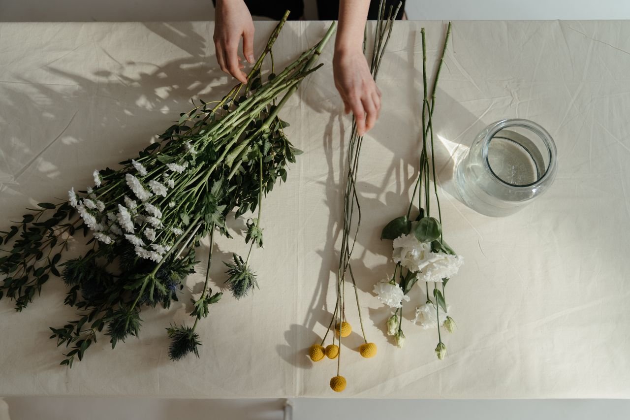 Hands arranging a bouquet of flowers on a beige table, perfect for floral arrangement themes.