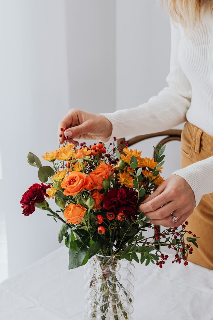 Elegant floral arrangement in a vase with autumn colors by woman indoors.